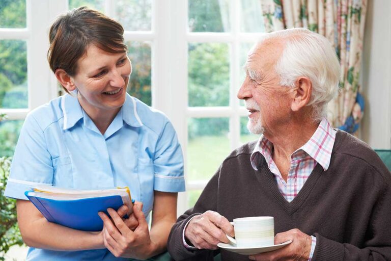 Older adults seated in a bright activity room doing gentle movement and music exercises with a caregiver.