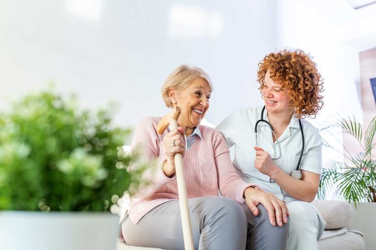 A group of older adults participating in a seated exercise class, smiling and gently stretching their arms.